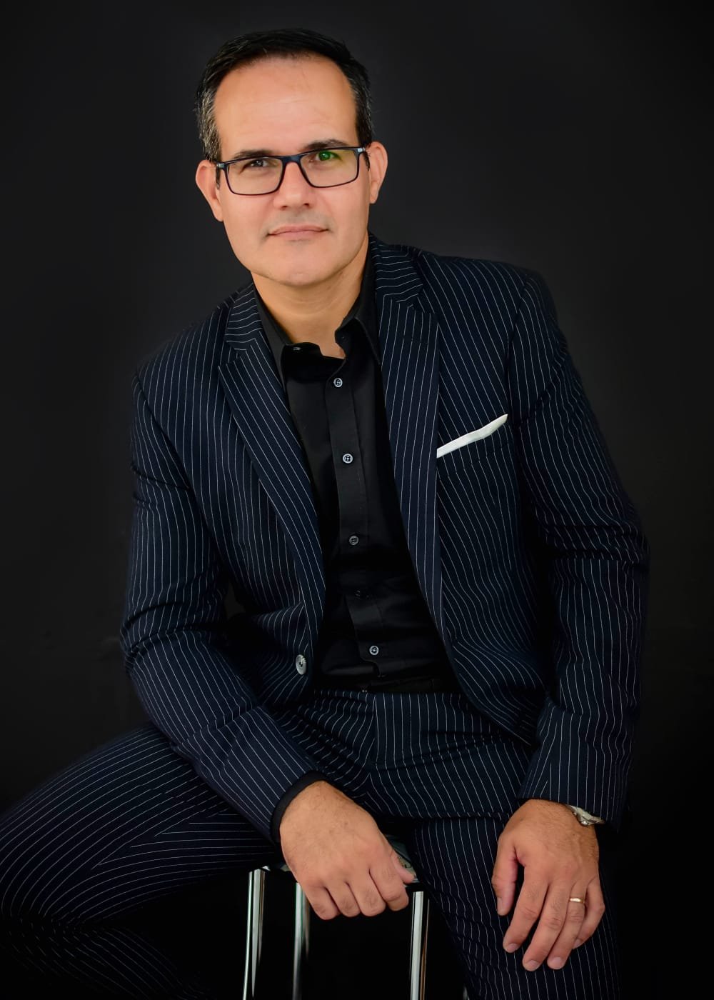 Dr. Rodrigo Schenckel, advogado previdenciário, sentado em retrato profissional com fundo escuro